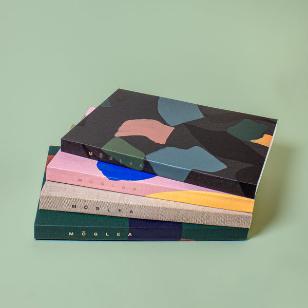 Stack of three green Moglea softcover medium A5 notebooks with blank pages, showcasing the textured covers and binding.